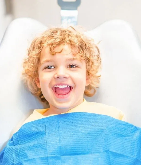 A young child sitting comfortably in a dental chair, smiling